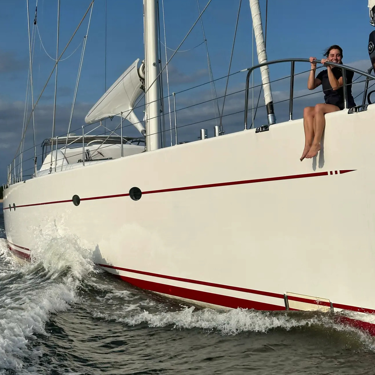 A gal sitting on the bow of a sailing yacht underway